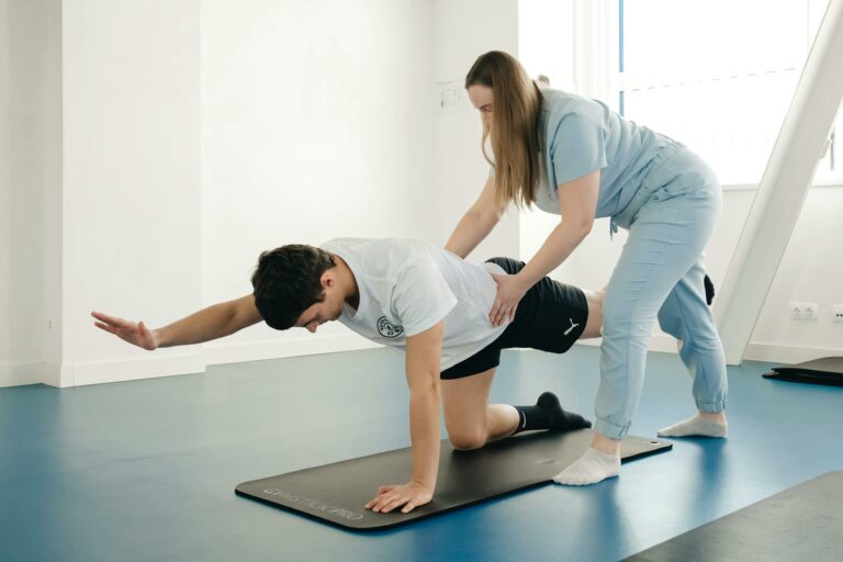 A physiotherapist guides a patient's exercise on a mat in a Vilnius gym.